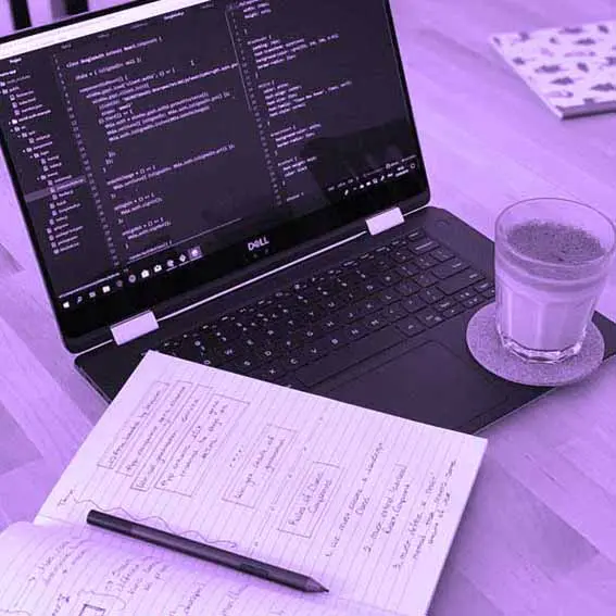 Photo d'un ordinateur avec du code sur l'écran, et un carnet ouvert.